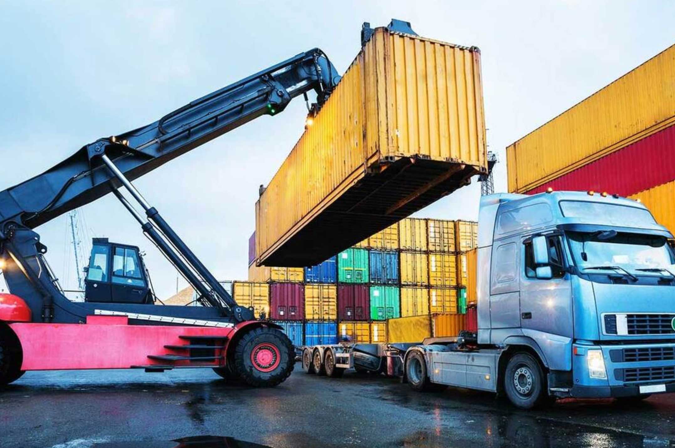 A shipping container being loaded onto a freight truck at a cargo yard